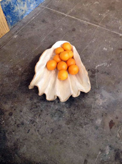 a sculpture on the floor in the shape of a large clamshell holds a pile of oranges